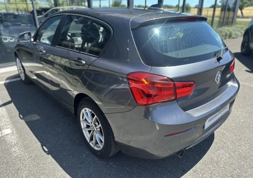 Vue 3/4 arrière droite d'une BMW Série 1 F20 gris foncé de 2019, avec feux arrière rouges et jantes alliage.