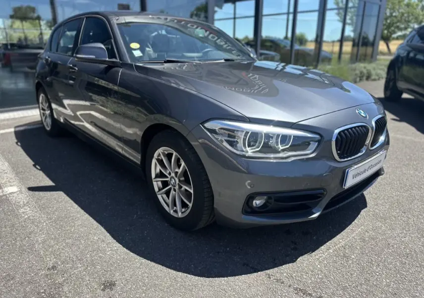 BMW Série 1 F20 gris foncé vue 3/4 avant droit, avec phares LED et calandre double haricot chromée.