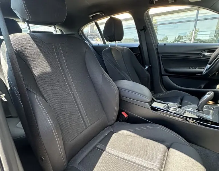 Vue intérieure côté conducteur de la BMW Série 1 F20 116D 2019 avec sièges tissu noirs et console centrale brillante.
