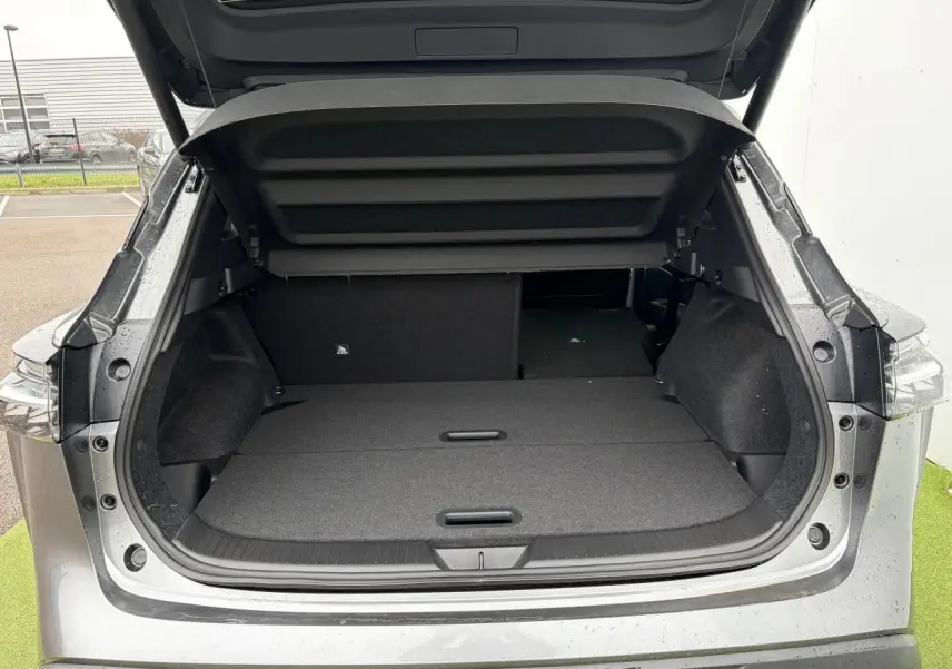 Coffre ouvert vu de l'arrière d'un Nissan Qashqai III gris foncé métallisé avec banquette arrière partiellement rabattue.