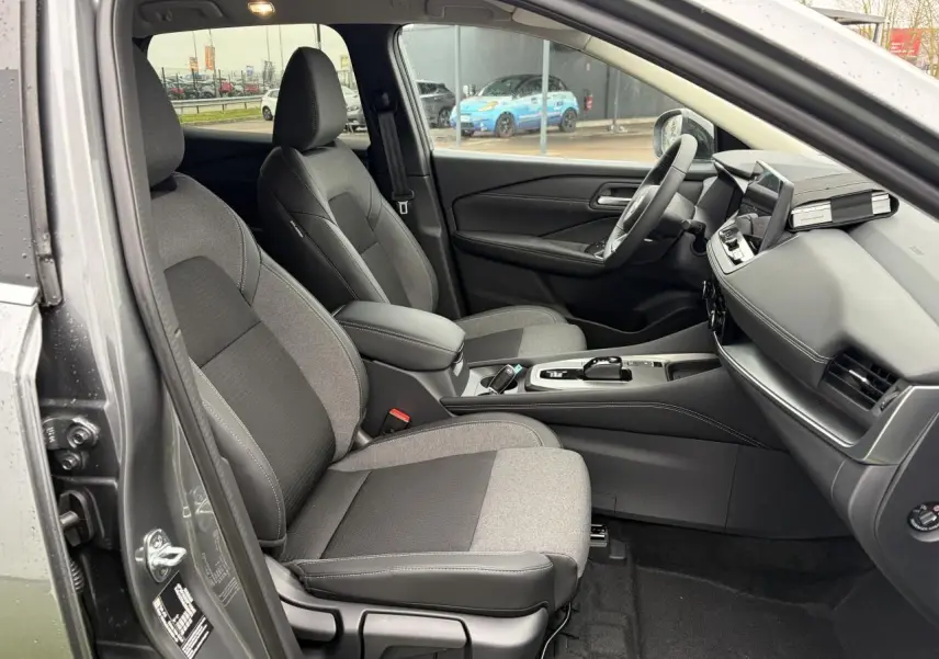 Vue intérieure côté conducteur du Nissan Qashqai III gris foncé, montrant les sièges avant et le tableau de bord moderne.