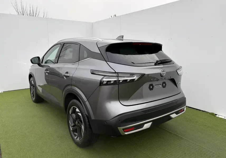 Vue 3/4 arrière droite du Nissan Qashqai 2025 gris foncé métallisé avec feux LED et barres de toit chromées.