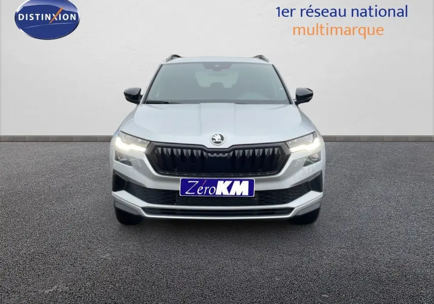 Vue frontale d'un Skoda Karoq gris argent métal 2025 avec calandre noire et feux allumés sur fond neutre.