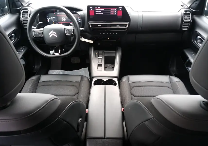 Vue intérieure avant du Citroën C5 Aircross 2023 avec tableau de bord noir, écran tactile central et sièges en tissu noir.