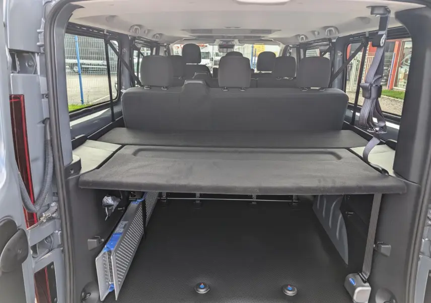 Vue arrière de l'intérieur du Renault Trafic Fourgon gris 2024 montrant la banquette et l'espace de chargement aménagé.