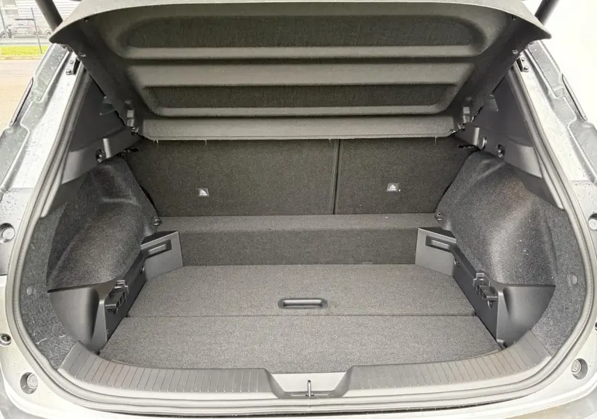 Coffre ouvert vu de l'arrière d'un Nissan Qashqai III 2025 gris foncé, espace de chargement vide et tapis gris.