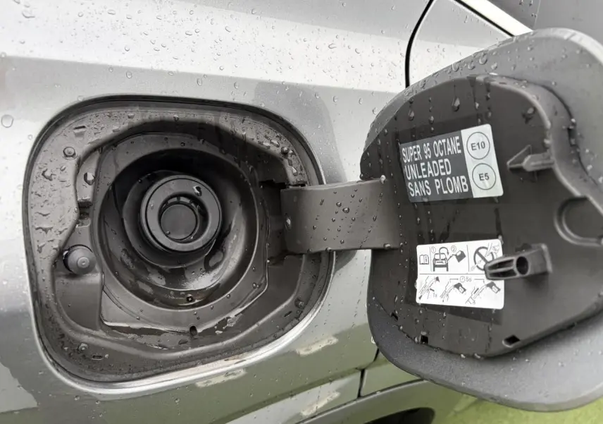 Gros plan sur la trappe à carburant ouverte du Nissan Qashqai 2025 gris foncé, avec étiquette essence sans plomb visible.