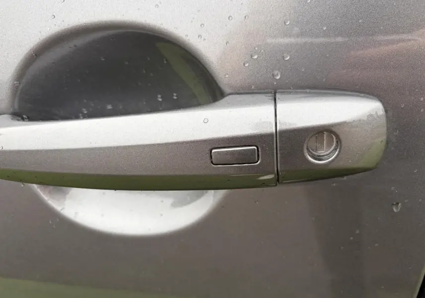 Poignée de porte avant droite gris métallisé du Nissan Qashqai 2025 avec bouton d'ouverture mains libres sous pluie.