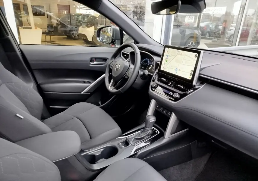 Vue intérieure côté conducteur de la Toyota Corolla Cross 1.8 hybride noire, avec écran tactile et volant multifonction.