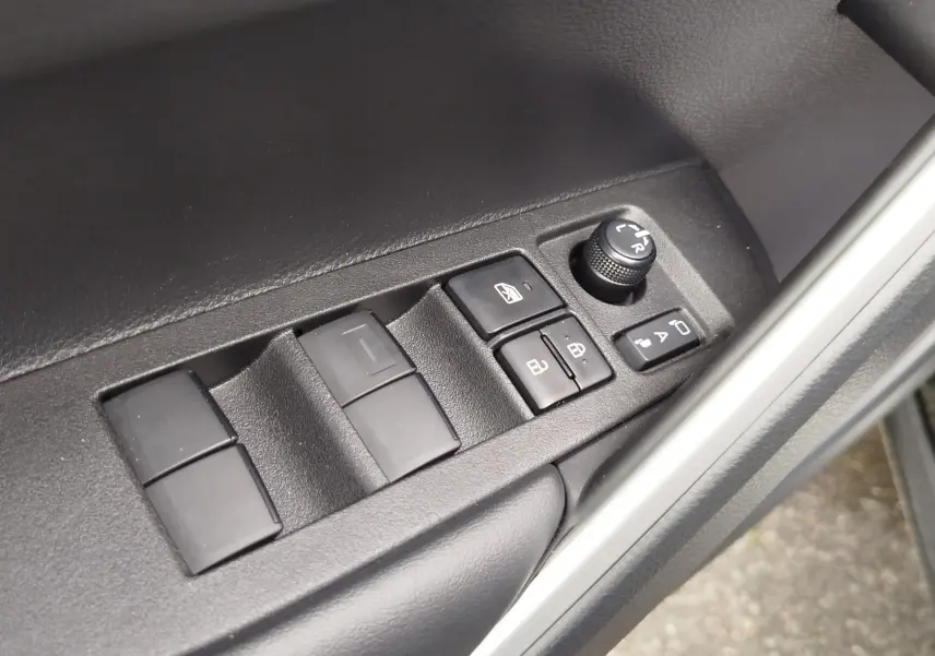 Gros plan sur les commandes de lève-vitres et réglage des rétroviseurs côté conducteur d'une Toyota Corolla Cross noir intense.