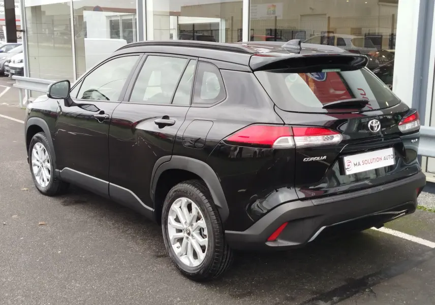 Vue 3/4 arrière droite d’un Toyota Corolla Cross noir intense avec jantes argent et feux arrière LED visibles.