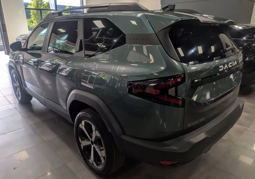 Vue 3/4 arrière droite du SUV Dacia Bigster vert cèdre avec jantes biton et feux arrière LED en showroom.
