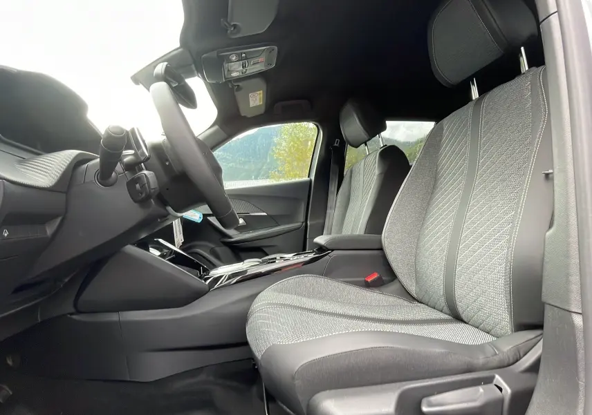 Intérieur du Peugeot 2008 2024, vue côté conducteur, sièges tissu gris avec surpiqûres et console centrale moderne.