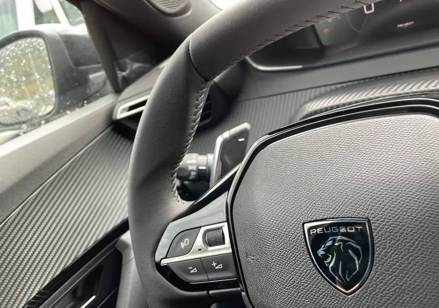 Gros plan sur le volant cuir noir avec logo Peugeot du 2008 Gris artense, mettant en valeur les commandes intégrées.