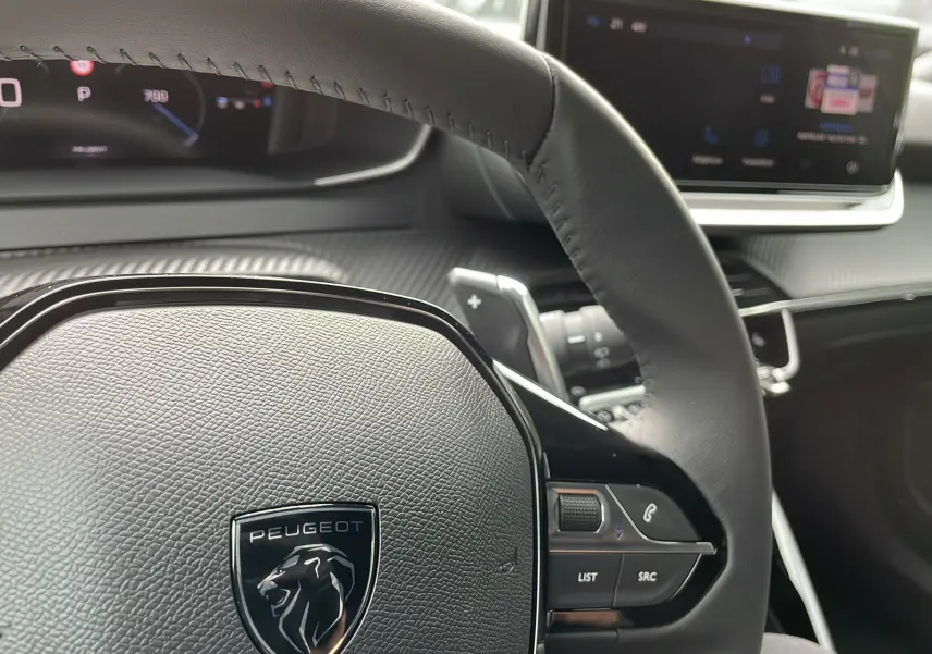 Vue rapprochée du volant cuir noir avec logo Peugeot et tableau de bord numérique du 2008 Gris Artense 2024.