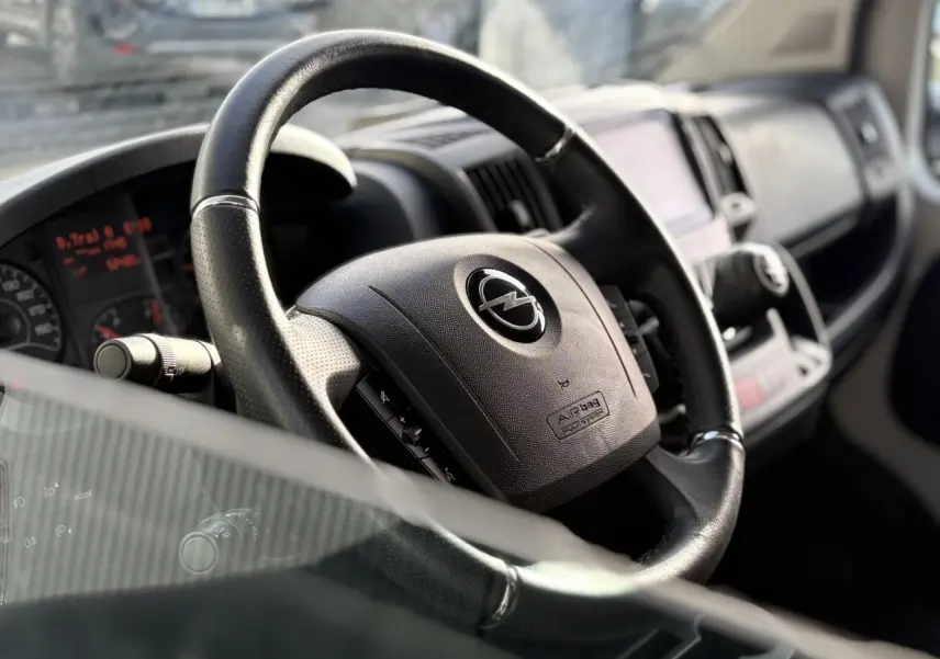Gros plan sur le volant noir de l’Opel Movano Fourgon 2024, avec tableau de bord et commandes visibles en arrière-plan.