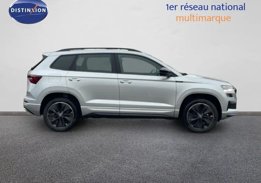 Vue de profil côté gauche d’un Skoda Karoq gris argent métallisé 2025 avec jantes noires bicolores et toit ouvrant.