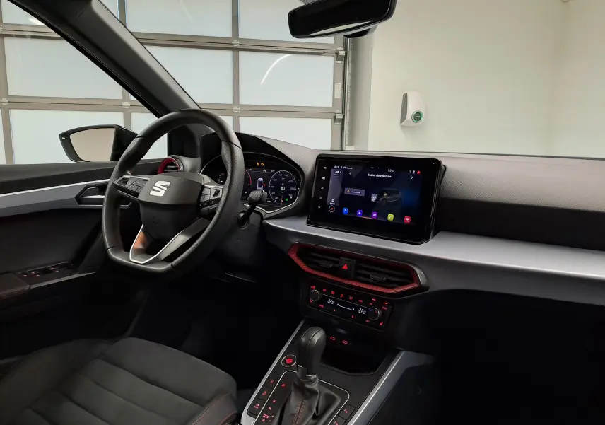 Vue intérieure côté conducteur du SEAT Arona 2024, tableau de bord moderne avec écran tactile et volant multifonction noir.