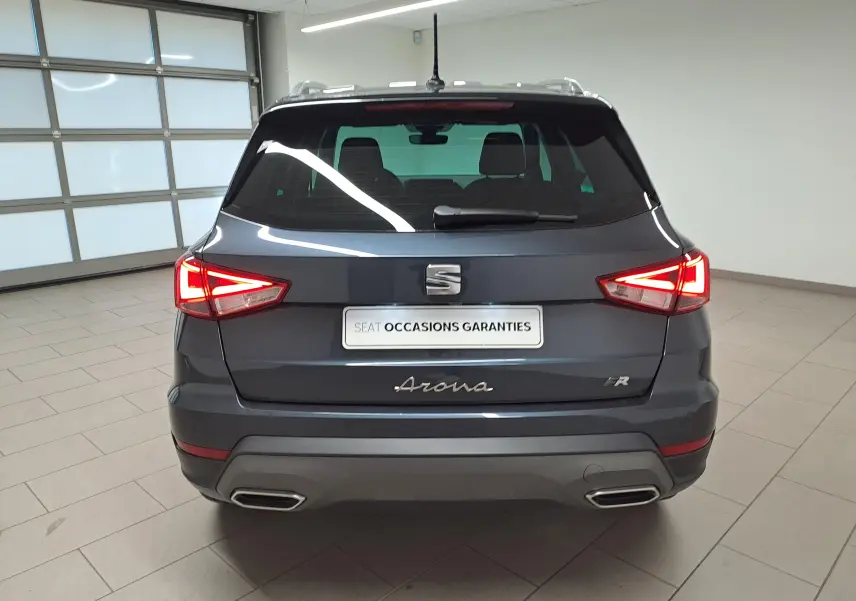 Vue arrière d'un SEAT Arona 2024 gris magnétique avec toit noir et feux arrière allumés en intérieur.