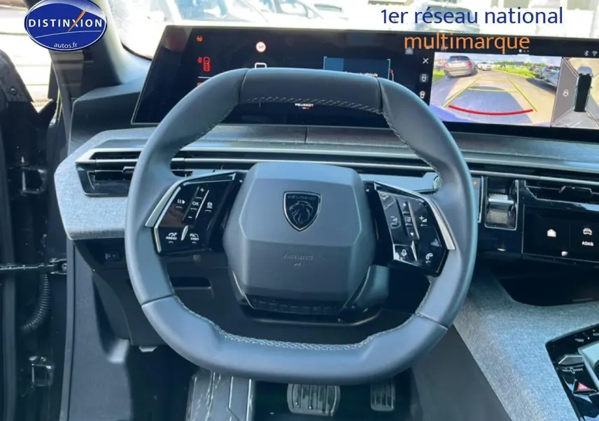 Vue intérieure centrée sur le volant cuir multifonction du Peugeot 5008 gris titane avec écran tactile et caméra de recul affichée.