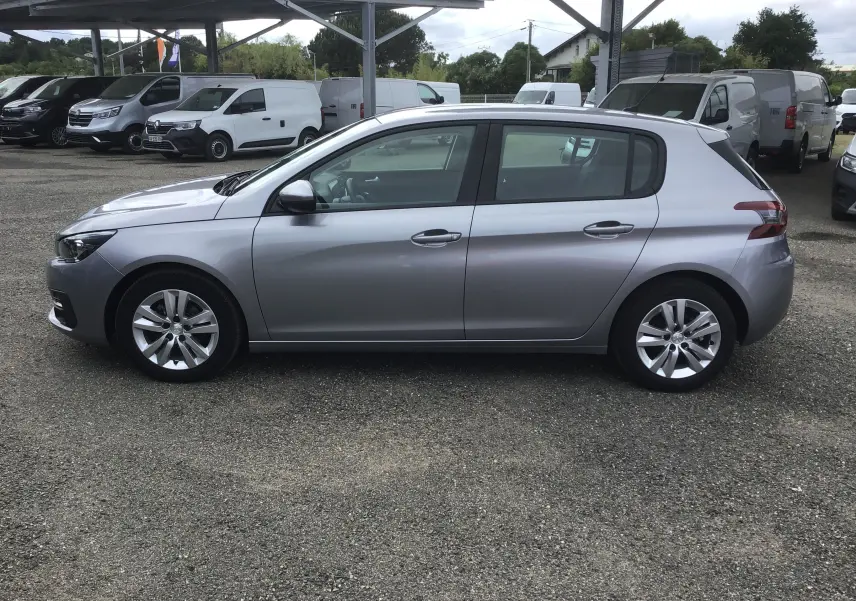 Vue de profil côté gauche d'une Peugeot 308 gris artense 2020 garée sur un parking extérieur sous un abri.