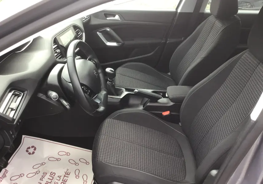 Vue intérieure côté conducteur de la Peugeot 308 1.5 BlueHDi gris Artense, sièges tissu à motif pied-de-poule et boîte manuelle.