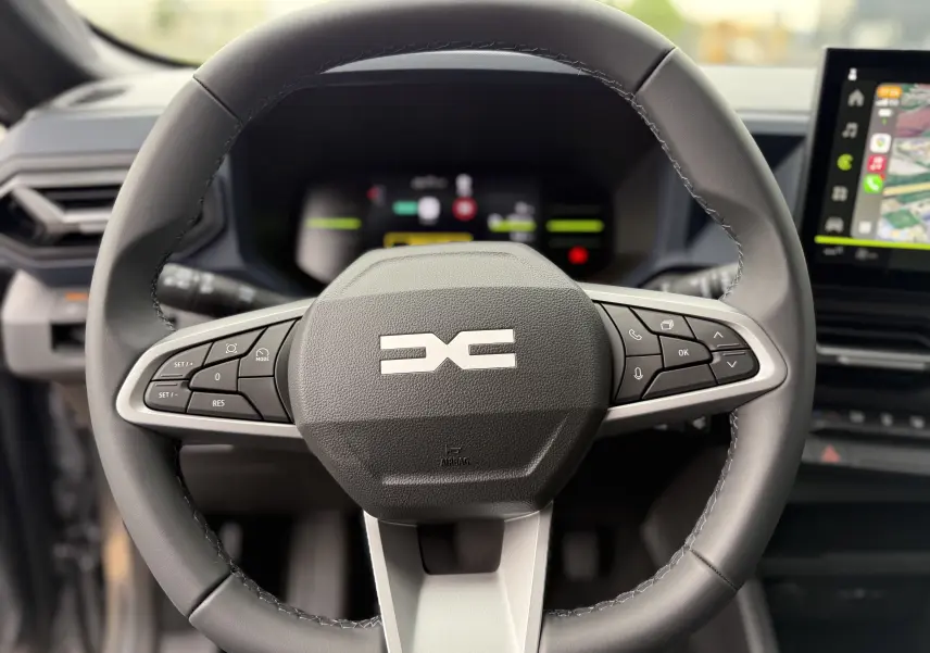 Gros plan sur le volant noir du Dacia Duster 2025 avec commandes intégrées et tableau de bord numérique flou en arrière-plan