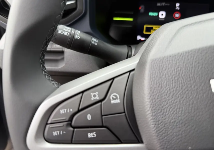 Gros plan sur les commandes au volant gris du Dacia Duster 1.6 Hybrid 140ch, avec tableau de bord numérique en arrière-plan.