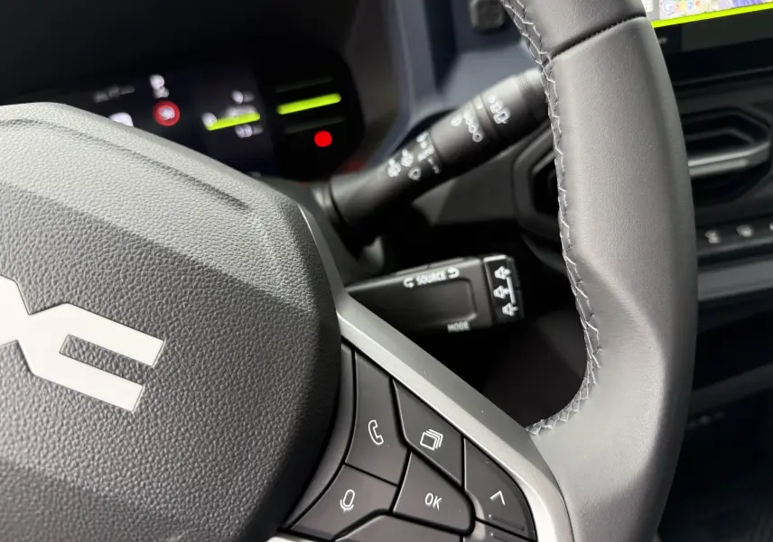 Gros plan sur le volant gris du Dacia Duster 2025 avec commandes intégrées et tableau de bord numérique en arrière-plan.