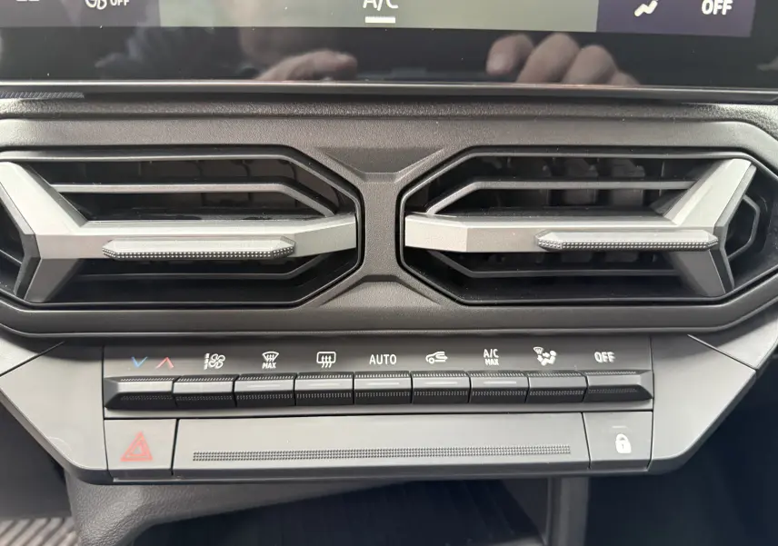 Détail de la console centrale avec les aérateurs hexagonaux et les commandes climatisation du Dacia Duster gris schiste 2025.