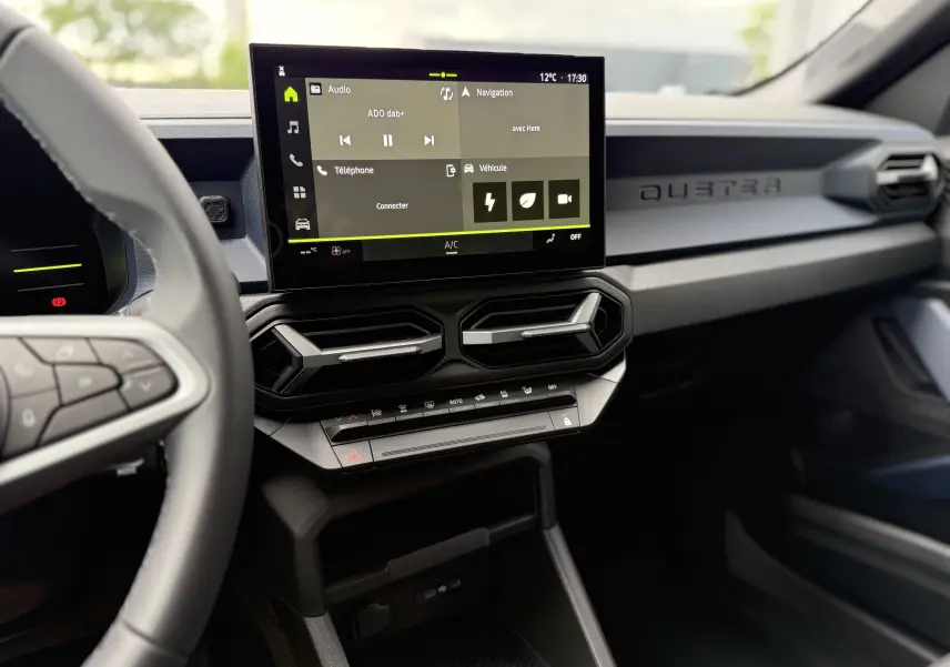 Vue intérieure du tableau de bord du Dacia Duster 2025 gris schiste, avec écran tactile central et commandes climatisation.