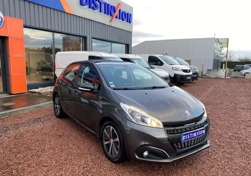 PEUGEOT 208 gris métallisé vue 3/4 avant droit, avec phares allumés et jantes alliage 16 pouces titane.