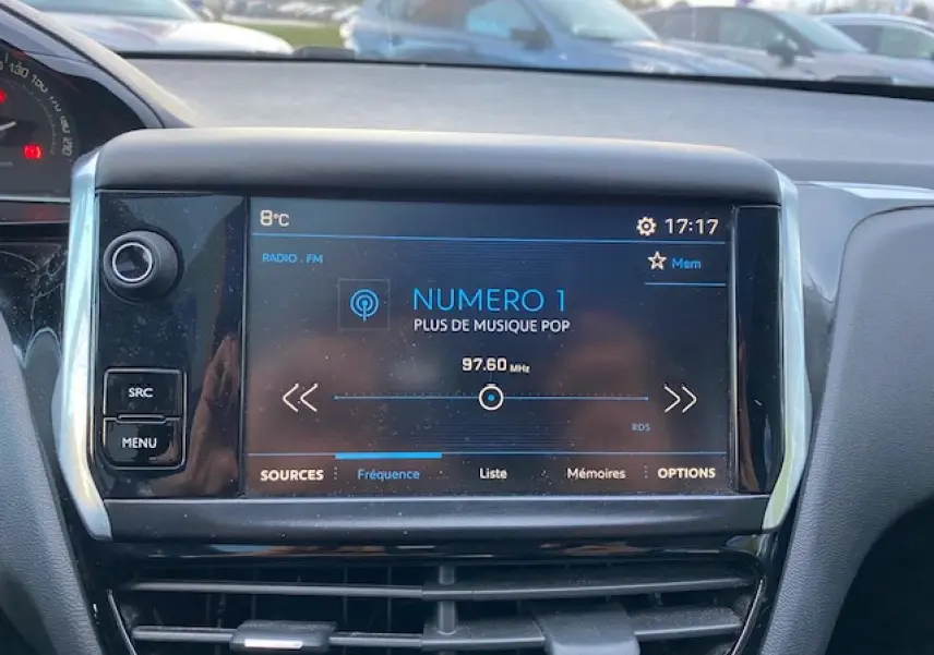 Écran tactile central affichant la radio FM dans l'habitacle d'une Peugeot 208 gris 2017 vue de face.