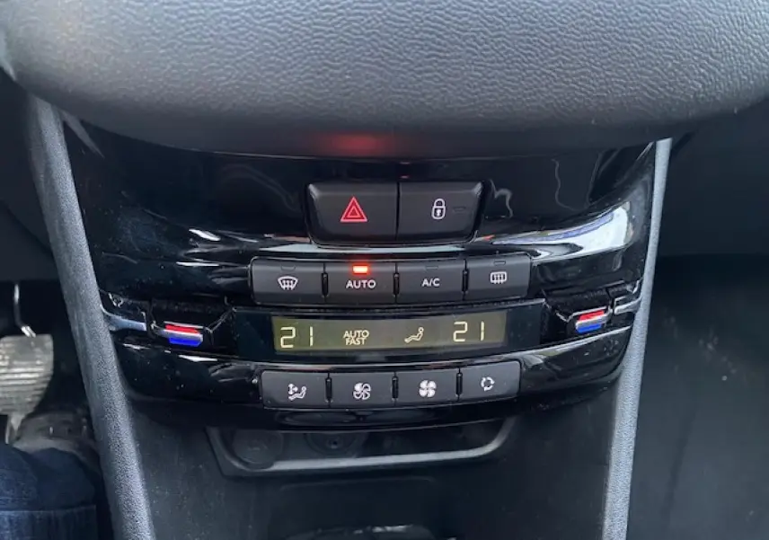 Gros plan sur la console centrale noire brillante de la Peugeot 208 gris, affichant la climatisation automatique à 21°C.