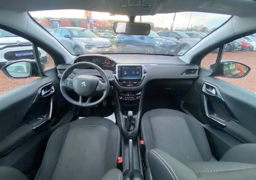 Vue intérieure avant de la Peugeot 208 gris 2017, montrant le tableau de bord, volant multifonction et sièges avant noirs.