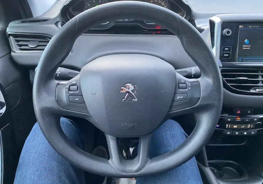 Vue rapprochée du volant multifonction noir d'une Peugeot 208 gris, avec tableau de bord et écran tactile visible.