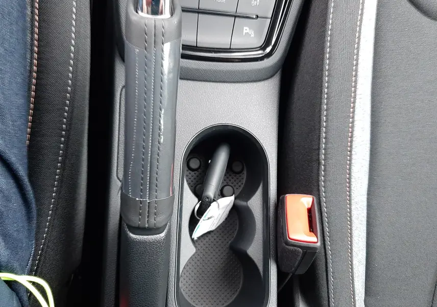 Vue plongeante sur la console centrale noire du Skoda Kamiq 2025 avec frein à main, porte-gobelets et ceinture de sécurité rouge.