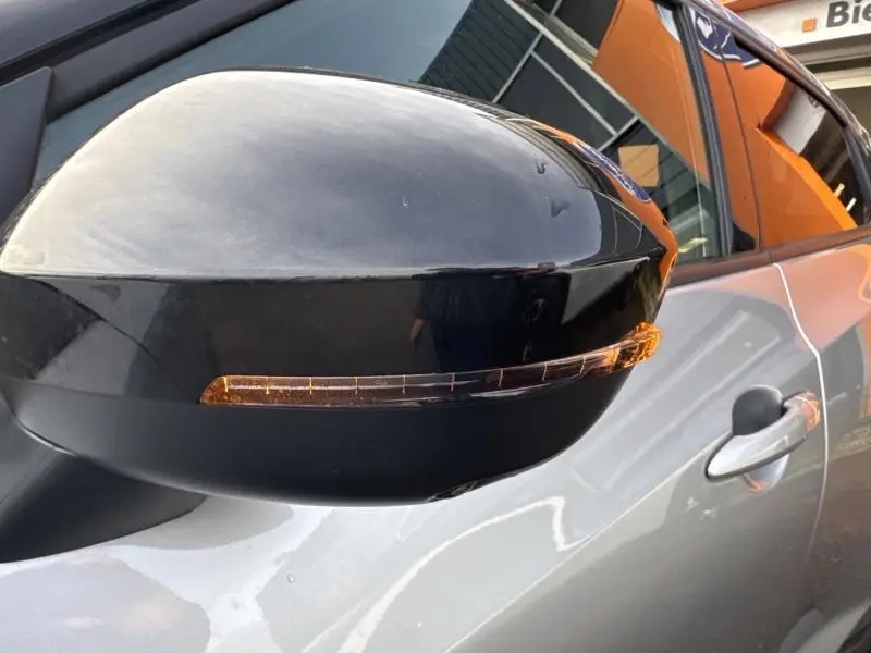 Rétroviseur droit noir brillant avec clignotant intégré sur Nissan Juke gris perle métallisé, vue rapprochée côté passager.