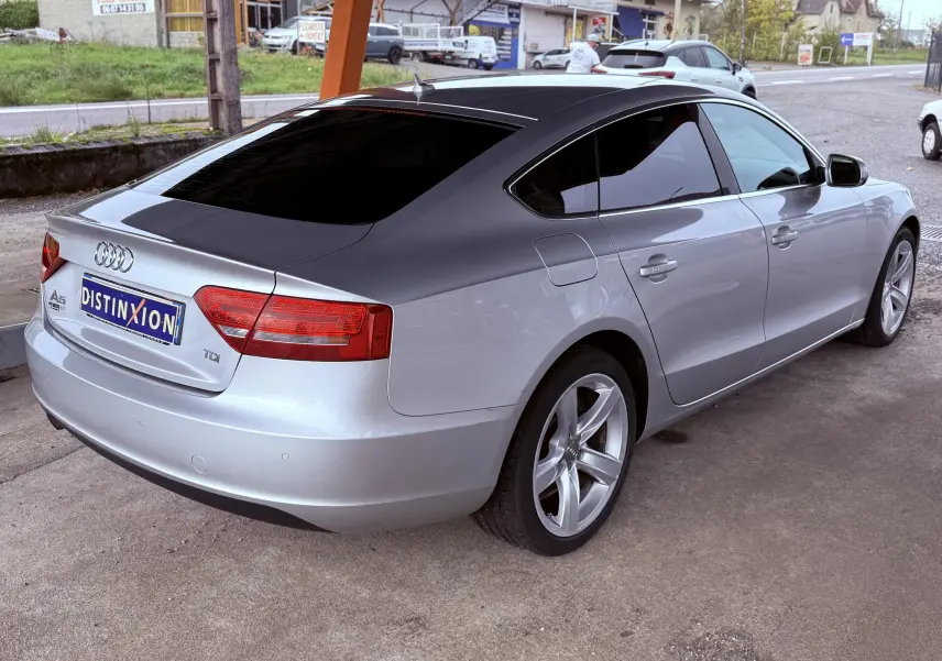 Audi A5 gris vue 3/4 arrière droit, toit noir et jantes alliage 5 branches, stationnée sur parking extérieur.