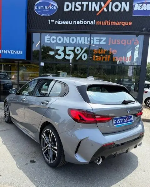 BMW Série 1 118d gris foncé vue 3/4 arrière droit, avec jantes alliage et feux arrière LED distinctifs.