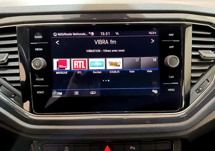 Écran tactile central allumé affichant les radios FM dans l’habitacle du Volkswagen T-Roc blanc.