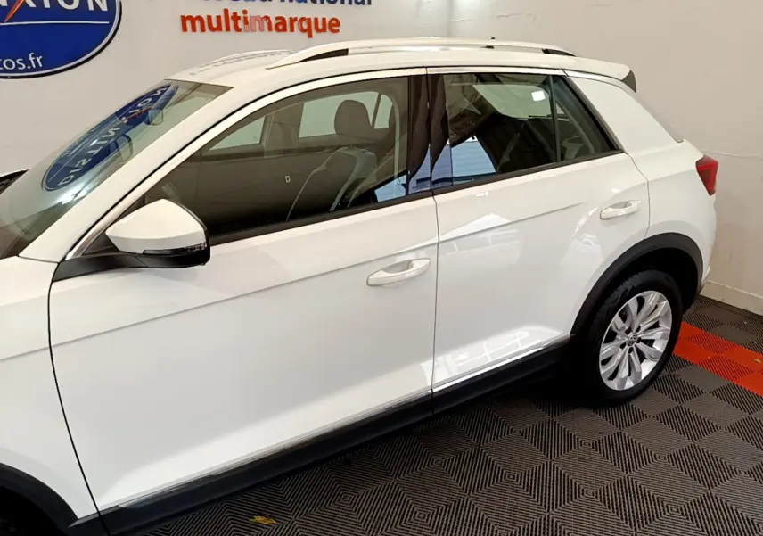 Vue latérale côté gauche d'un Volkswagen T-Roc blanc stationné en intérieur avec jantes alliage visibles.