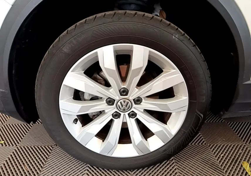 Gros plan sur la jante alliage argentée avec logo Volkswagen du Volkswagen T-Roc blanc, roue avant droite visible.
