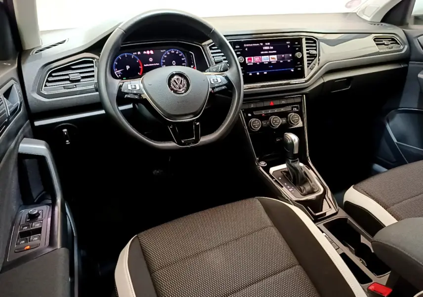 Vue intérieure du tableau de bord et volant cuir noir du Volkswagen T-Roc 1.5 TSI 150 EVO Carat avec écran tactile central.