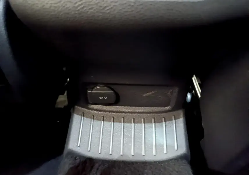 Prise 12V noire en gros plan sous le tableau de bord du Volkswagen T-Roc blanc, intérieur sombre.