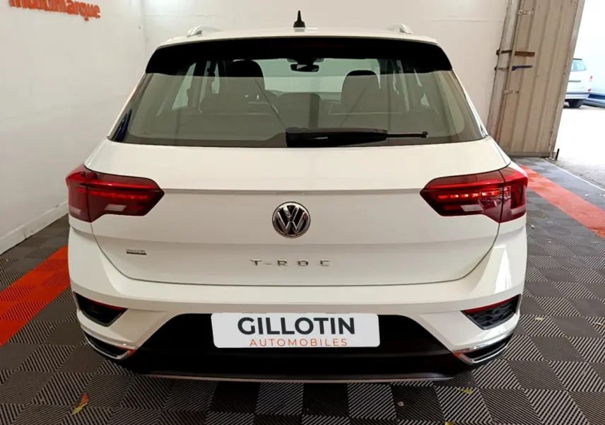 Vue arrière d'un Volkswagen T-Roc blanc avec feux arrière allumés et logo VW bien visible.