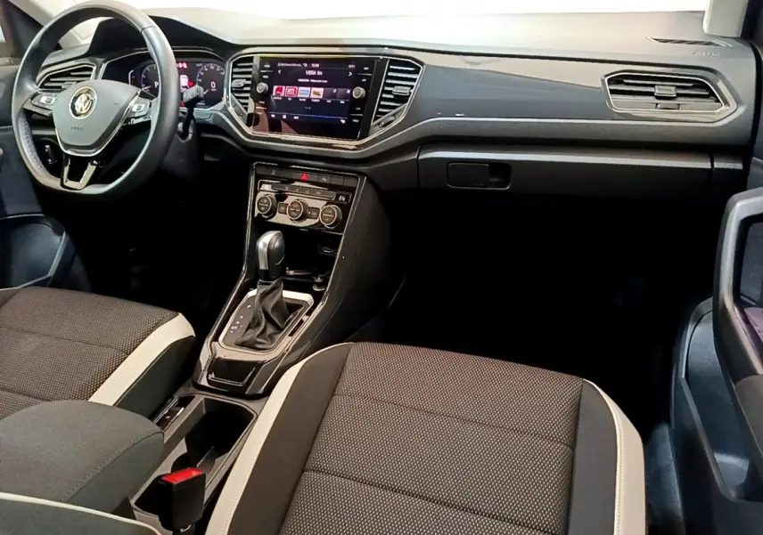 Intérieur avant du Volkswagen T-Roc 1.5 TSI blanc, tableau de bord moderne avec écran tactile et sièges bi-ton noirs et beige.