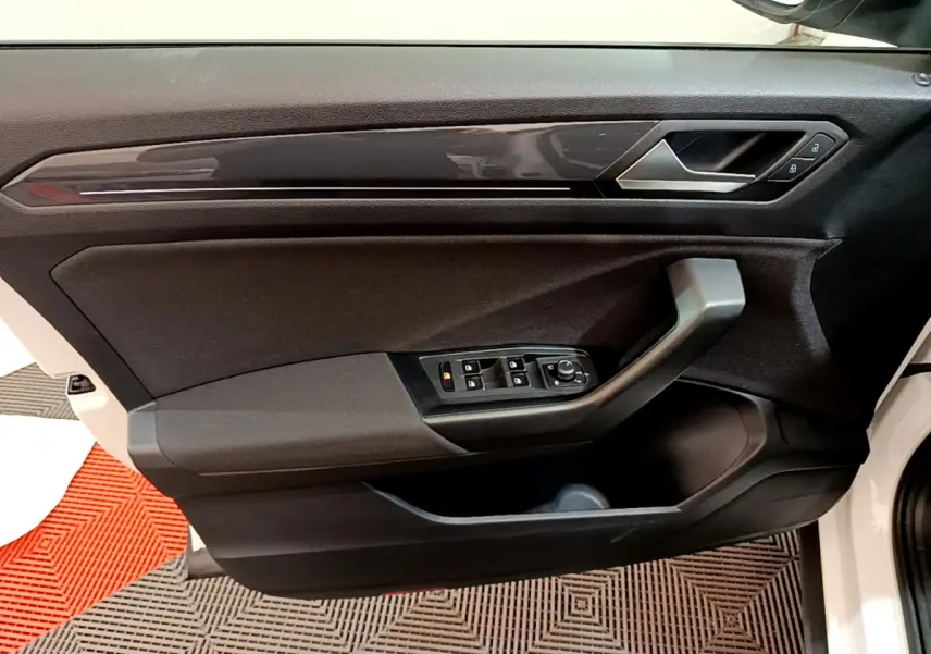 Vue rapprochée de la porte avant gauche du Volkswagen T-Roc blanc, avec commandes électriques et poignée intégrée.