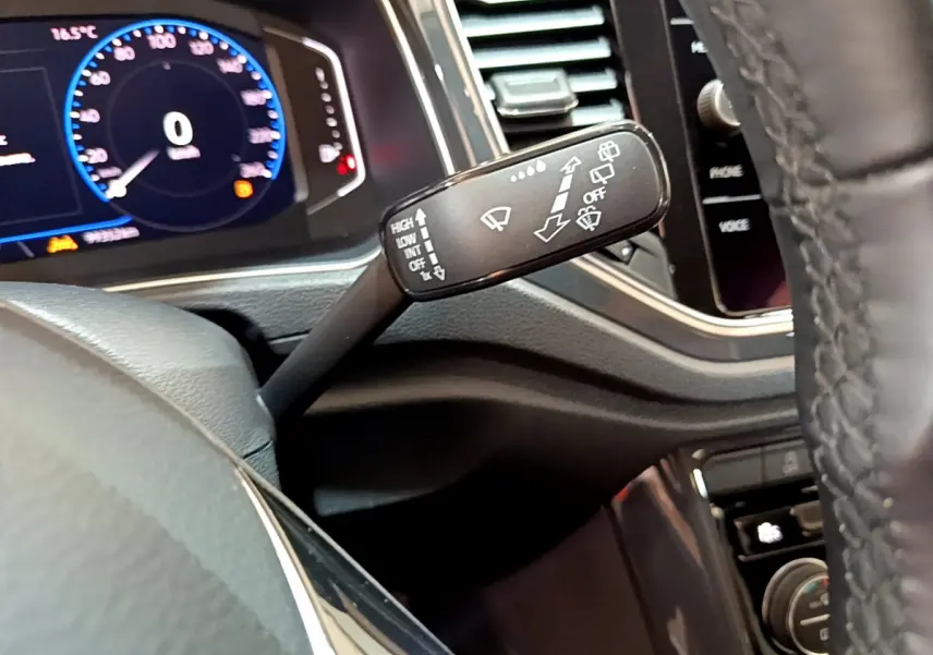 Gros plan sur la commande d’essuie-glace à gauche du volant cuir du tableau de bord numérique du Volkswagen T-Roc blanc.