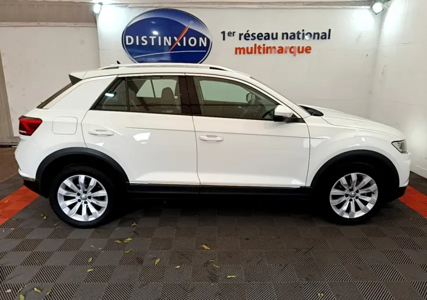 Profil droit du Volkswagen T-Roc blanc 2020 avec jantes alliage et barres de toit chromées en intérieur showroom.